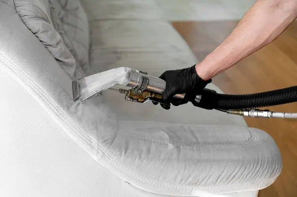 Rahat bir oturma odasında döşeme temizleme makinesi kullanarak açık renkli bir kanepeyi temizlemek ve restore etmek.