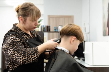 Yetenekli bir stilist, şık bir saç kesimine parlak, hoş geldin ortamında odaklanır. Genç müşteri rahatça oturuyor, yeni bir görünüme hazır..