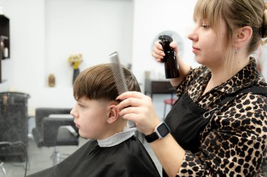 Yetenekli bir kuaför zarif bir kuaförde bir çocuğun saçını titizlikle keser, hassasiyetini ve bakımını gösterir. Sıcak atmosfer genç müşteri için hoş bir ortam yaratıyor..