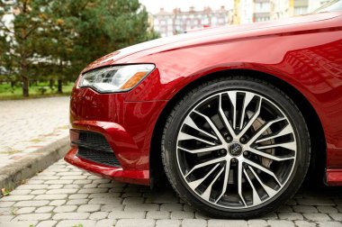 Ivano-Frankivsk, Ukrayna 12 Ekim 2023: Aydi A6 arabası, sedan. Kırmızı bir Aydi A6 kaldırım taşı bir caddeye park edilmiş, parlak tasarımı ve parlak alaşımlı tekerlekleri sergileniyor. Arka planda çağdaş binalar ve verimli yeşillikler var.