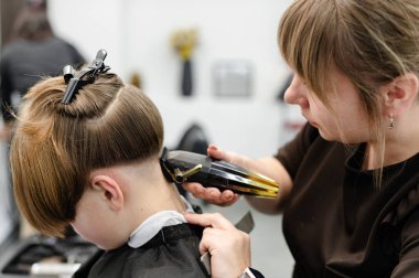 Yetenekli bir stilist, çağdaş bir salonda bir çocuğun saçını dikkatlice kesiyor. Atmosfer canlı, modern mobilyalar ve parlak ışıklandırma deneyimi geliştiriyor..