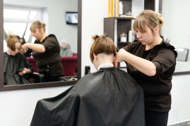 Yetenekli bir stilist, çağdaş bir kuaförde müşterisinin saçını kesiyor. Sahne aynaları, saç aletleri ve rahat bir atmosfer sergiliyor. Her iki şahıs için de canlı bir deneyim yaratıyor..
