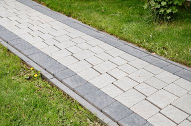 Gri ve açık taştan yapılmış düzgün bir kaldırım yolu yemyeşil bir çimenliğin içinden geçiyor. Taze otlar yolu kapatır ve yerleşim ortamında davetkar bir açık hava alanı yaratır. Profesyonel kaldırım taşı temizliği.