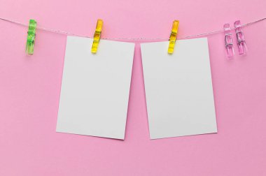 Sarı, yeşil ve pembe renkli parlak mandallar pembe bir arkaplana karşı boş notlar iliştirir, mesajlar, hatırlatıcılar veya yaratıcı göstergeler için idealdir.