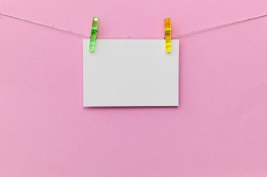 İki renkli klip arasında parlak pembe bir zemin üzerinde boş bir kart asılı. Bu ayar yaratıcı mesajlar ve çeşitli durumlar için dekorasyonlar için mükemmeldir..