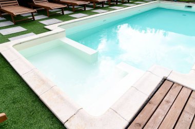 Hoş bir yüzme havuzu, şezlonglar ve açık havada yemyeşil bir ortam.