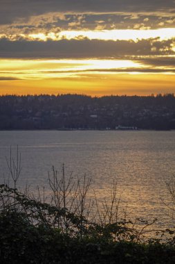 Gün batımı, katmanlı bulutlarla birlikte suyun üzerinde parlıyor.