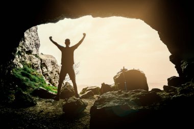 Mağarada muzaffer kolları olan bir adamın silueti..