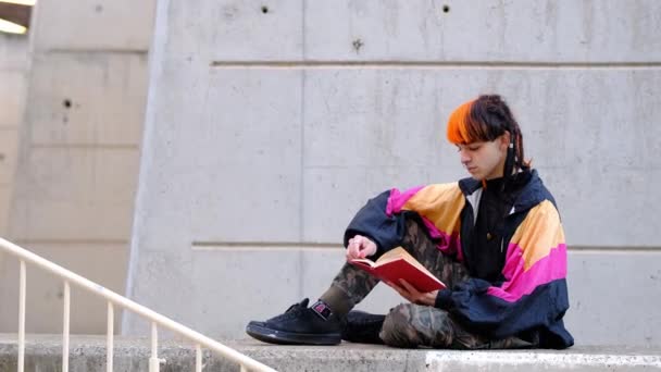 Junger Mann Mit Orangefarbenen Und Schwarzen Haaren Liest Ein Rotes — Stockvideo