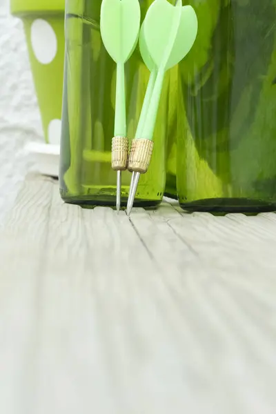Green darts on a target with beer bottles in the background.