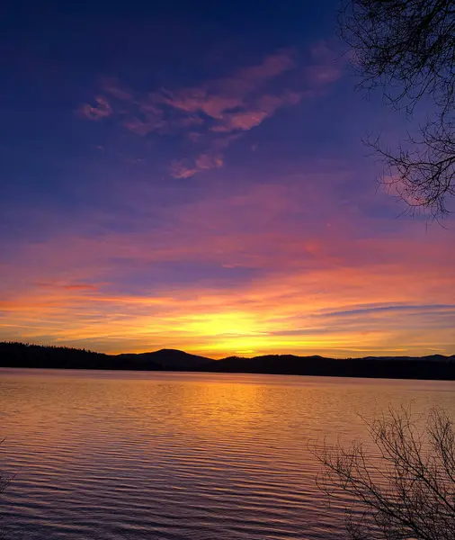 Karanlık, renkli gökyüzü ve dağ siluetinin yer aldığı bir gölün üzerinde cesur bir günbatımı. 