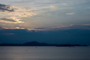 Sakin sular, uzak adaların ardında güneş batarken alacakaranlığın güzel tonlarını yansıtır. Bu sakin sahil sahnesinde tekneler yavaşça sallanıyor..
