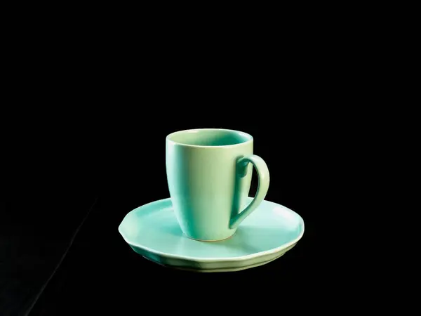 Nane yeşili kahve fincanı, siyah kumaş arka planına yerleştirilmiş, uyumlu bir fincan tabağında.