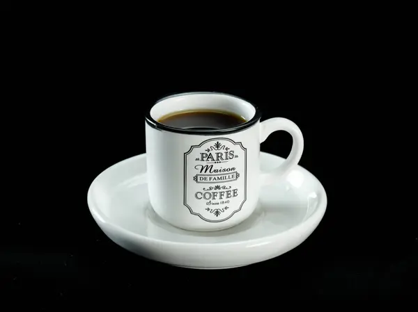 Beyaz seramik kupa, klasik Paris tasarımı, siyah kumaş arka planına karşı uyumlu bir çay tabağı üzerine yerleştirilmiş.