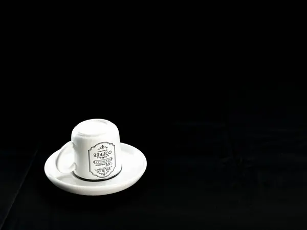 Beyaz seramik kupa, klasik Paris tasarımı, siyah kumaş arka planına karşı uyumlu bir çay tabağı üzerine yerleştirilmiş.