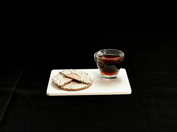 Bir bardak sıcak kahve geleneksel Meksika usulü çikolatayla eşleştirildi ve beyaz mermer bir tahtada siyah bir fonda duran kaşık ile pohpohlandı.