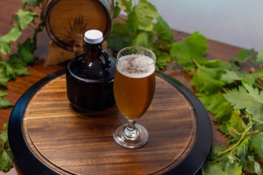 Tahta bir masada, bira bardağında taze bira, bira fıçısı gibi elementler ve zıplama yaprakları, otantik bir bira havası yaratır.