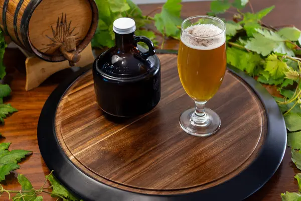 Geleneksel meşe fıçısının yanında lale bardağında servis edilen taze bir zanaatkar birası ve ev yapımı temalar için mükemmel koyu cam bir homurdanma.