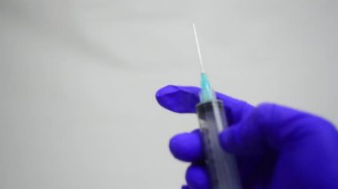 Aşı sıvısını şırıngayla şişeye koymaya hazırlanan bir doktorun eli. Tıbbi eldivendeki izole el beyaz arka planda bir şırınga enjekte etmeye hazırlanıyor. Elin şırıngayı tutuyor. Tıp ve sağlık kavramı.