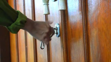 Kapı kollarını anahtarla açarken elinizi kapatın. Anahtarı ve kilidi kullanan kişi. Bir adamın elinin ön kapısını açarken, anahtar, yan görüş, kapıyı açar ve odaya girer, yakın plan statik çekim. ahşap kapı