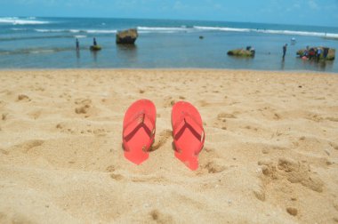 Plaj kumu arka planı - Tropikal kumsalda parmak arası terlikler - yaz tatili seyahat konsepti - Kopya alan. Kırmızı lastik plaj terlikleri kumsalda gömülü. Seçici odaklanma. Konsept: deniz veya okyanus kenarında tatil