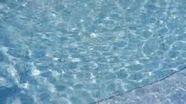 Mavi yüzeyi olan bir yüzme havuzu. Atmosfer sakin ve sakin, su sakin ve huzurlu görünüyor. Kristal berraklığında su, havuzda güneş ışığıyla dalgalanır. Güzel bir arkaplan.