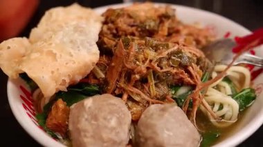 Bir adamın ellerinin yakın çekimi sosu ve çorbayı eşit bir şekilde karıştırmak için bir kase tavuklu erişteyi karıştırır ve yemek masasında yemek için yemeği hazırlar..