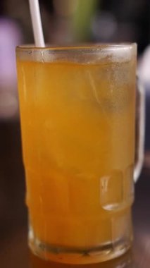 Buzlu taze portakal suyu. Sağlıklı içecek içecekler. Dikey video. Elle karıştırılmış buzlu portakal suyu ile saman. Portakal suyunu buz ve samanla karıştırmak