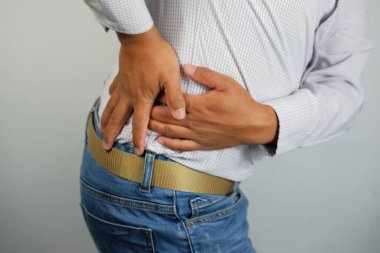 Sırt ağrısı, evde çalıştıktan sonra bel ağrısı çeken genç bir adamın yakın çekimi. Yetişkin bir adam belini tutuyor ve kronik sırt ağrısı çekiyor. Sağlık ve tıbbi bakım kavramları