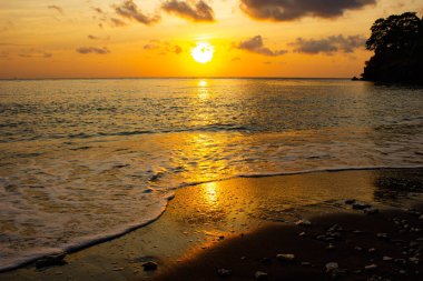 Sahilde dramatik turuncu gün batımı. Sahilde siyah kumlar. Bali Adası, Endonezya.