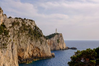 Yunanistan 'ın Lefkada Burnu' ndaki ikonik deniz fenerinin nefes kesici manzarası engebeli uçurumların tepesine tünemiş ve ılık akşam ışığında parıldayan İyon Denizi ile çevrili..