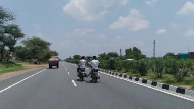 16 Aralık 2022 NH 52, Rajasthan, Hindistan. İki Hintli adam bir otoyolda başka bir motosiklete basarak motosiklet çekiyor..