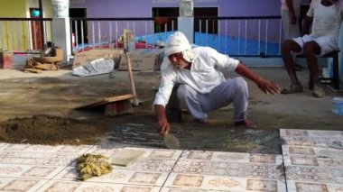 20 Aralık 2022 Reengus, Rajasthan, Hindistan. İnşaatçı zemine fayans yapıştırıcısı hazırlayıp yayıyor.