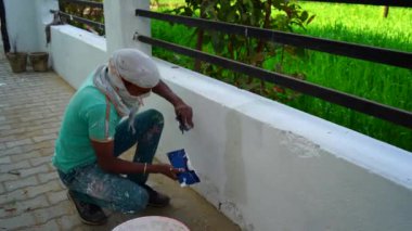 20 Aralık 2022 Rajasthan, Hindistan. Yakışıklı genç ressam boya silindiriyle duvar boyuyor ve kameraya gülümsüyor.