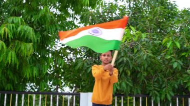 Bağımsızlığı ya da Cumhuriyet Günü 'nü kutlayan Hintli çocuk arka planda yeşil ağaçla el sallıyor ya da koşuyor..