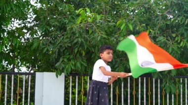Bağımsızlığı ya da Cumhuriyet Günü 'nü kutlayan Hintli çocuk arka planda yeşil ağaçla el sallıyor ya da koşuyor..
