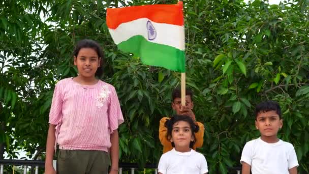 インドの子供たちは 屋根と緑の木の背景に旗を振って走っています インドの独立または共和国の日を祝うインドの子供 — ストック動画