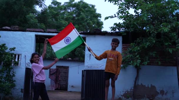 两个印度小孩在庆祝独立日或国庆日 可爱的印度小孩拿着 挥动或带着三色旗跑步 后面是房屋建造 — 图库视频影像