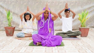 Lotus duruşu. Genç anne ve küçük ergen gözleri kapalı ve dua jestleriyle evde yoga yapıyorlar.