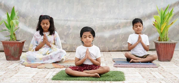 Yerdeki Hintli çocuklar evde yoga ve meditasyon yapıyorlar. Çocuklar dua pozisyonunda.