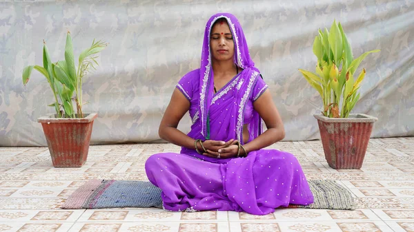 Indian village woman in traditional costume doing yoga or meditation on the roof at home.
