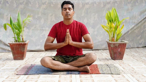 Spor kıyafetli genç adam yoga yapıyor ve bir egzersiz paspası üzerinde stüdyo grubuna karşı meditasyon yapıyor.