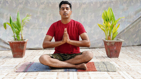 Young man in sporty outfit doing yoga and meditating on an exercise mat against a studio backgroun