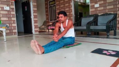 Kot pantolonlu Asyalı adam yerde oturup yoga pozunda meditasyon yapıyor.