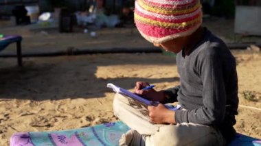 İlkokul öğrencisi dışarıda ödev yapıyor. Zavallı çocuklar kitap okuyor ve kalemle yazıyor..