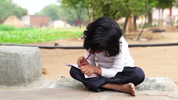 村里的小女孩在笔记本里做作业 坐在羊场附近的地上 印度农村镜头 — 图库视频影像