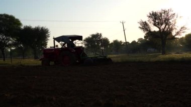 Traktör geniş tarlalarda sürerek tohumları saflaştırmak için özel yataklar yapıyor. Tarım aracı Hindistan kırsalında gün batımında çalışır. 25 Kasım 2023 Jaipur, Rajasthan, Hindistan.