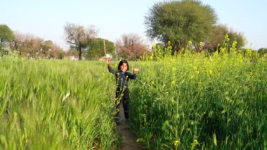 Gün batımında çimenlerin üzerinde oynayan, zıplayan ve koşan gülümseyen kızın portresi. El sallıyor. Parlak ışık arka planında alan. Haying zamanı.