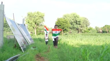 Ulusal bayrak logosu tasarımı giyen Hintli köylüler tişört basıp tutuyorlar, arka planda yeşillik olan Tricolor 'la el sallıyorlar, Bağımsızlık Günü' nü veya Cumhuriyet Günü 'nü kutluyorlar.