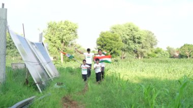 Elinde Hint bayrağı olan bir grup şakacı köy çocuğu darı tarım alanında - bağımsızlık konsepti veya cumhuriyet günü kutlaması, demokrasi ve özgürlük